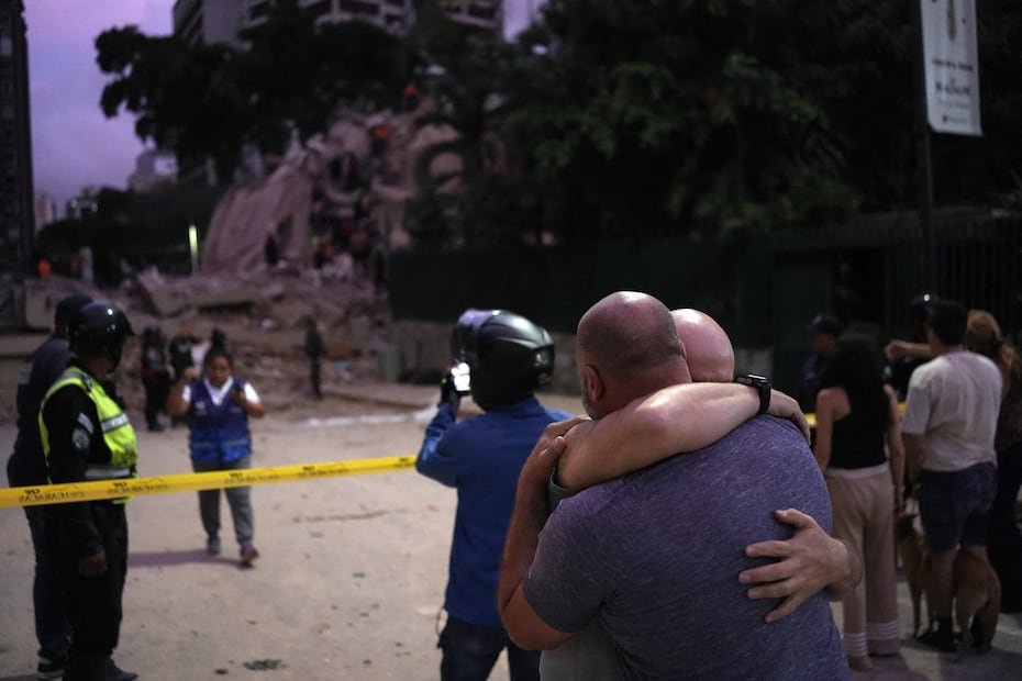 Hombres reaccionan frente a un edificio derrumbado.
