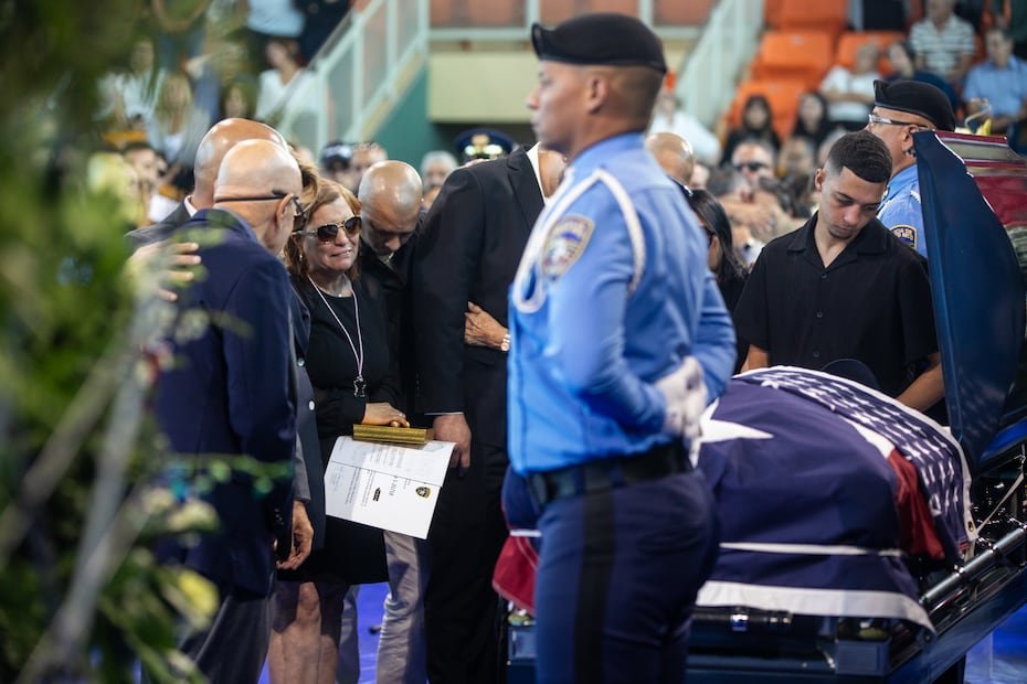 En el coliseo donde se realizaban los actos, la escena era profundamente conmovedora. El féretro de Santiago Renta, de 43 años, ocupaba el centro, cubierto con la bandera de Puerto Rico, rodeado por arreglos florales y por una guardia de honor que se mantenía firme.