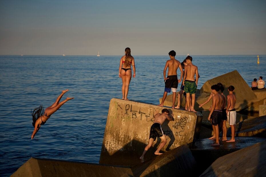 También en Barcelona, jóvenes bañistas saltan al agua desde una roca.