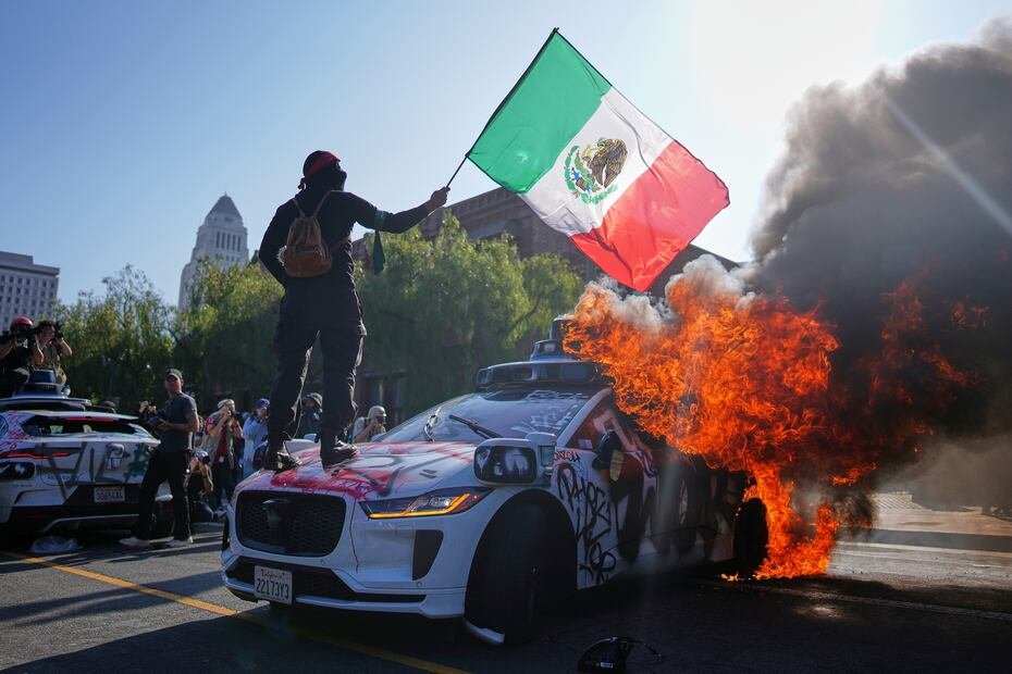 Un manifestante ondea la bandera de México mientras se para encima de un carro incendiado de la Policía durante las protestas.