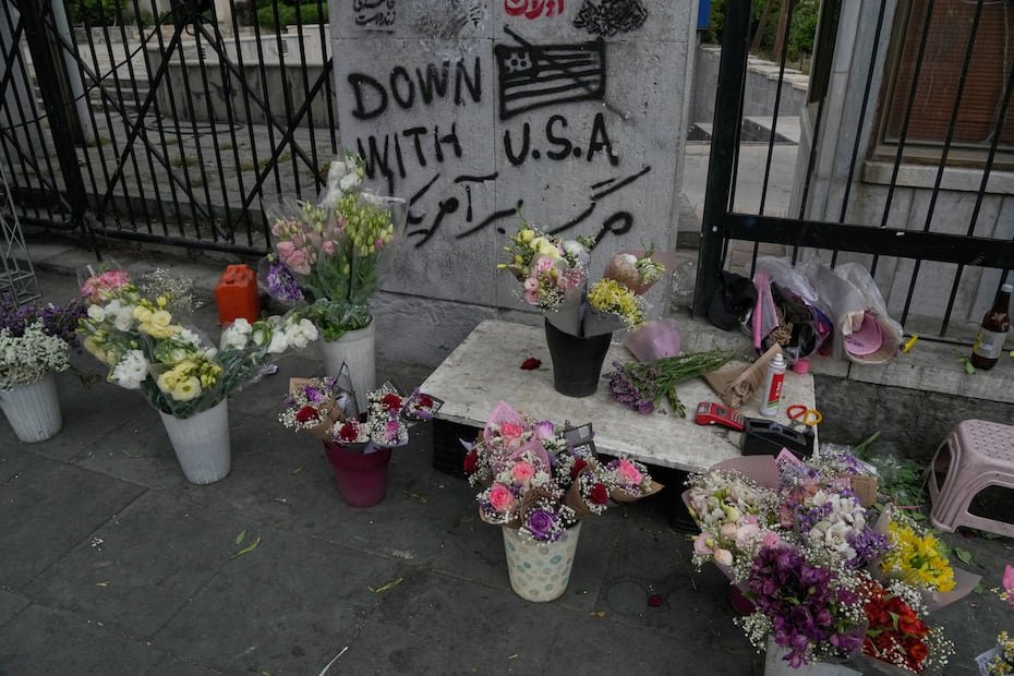Un grafiti antiestadounidense está pintado en una pared mientras un vendedor callejero exhibe flores en el centro de Teherán en Irán.