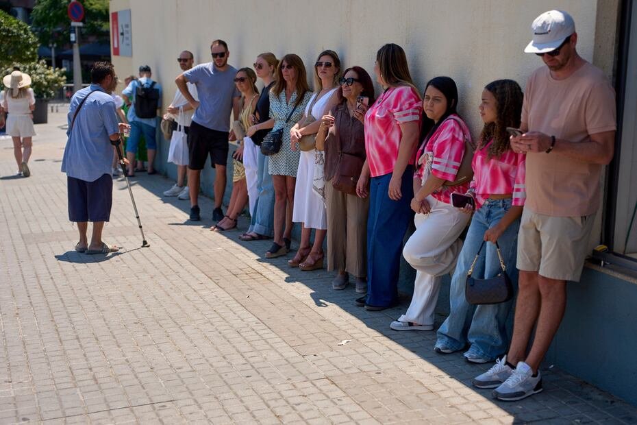 Un hombre pide dinero a personas que se resguardan en la sombra de una pared en Barcelona, cerca de la Sagrada Familia.
