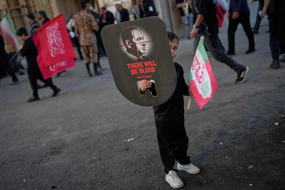 Un niño se asoma por detrás de un cartel que muestra al primer ministro israelí, Benjamin Netanyahu, con una mira telescópica y las palabras "habrá sangre" superpuestas.