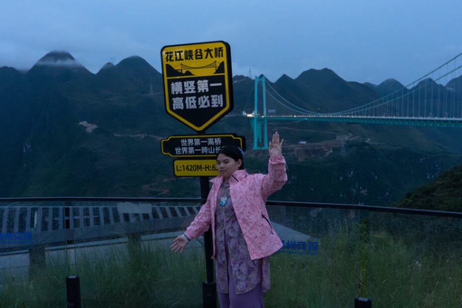 Una turista posa cerca de un cartel que promociona el puente del Gran Cañón de Huajiang como el de mayores dimensiones y longitud del mundo.