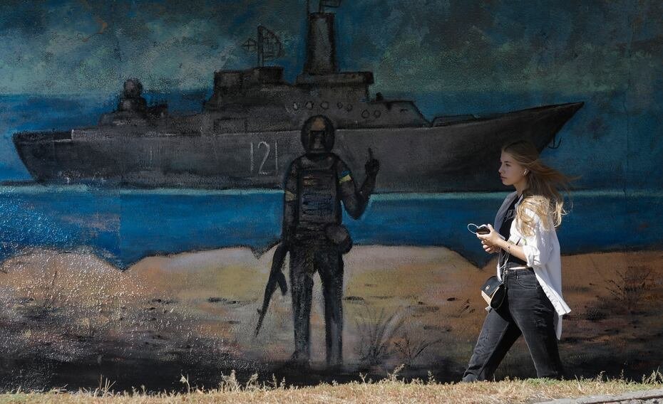 Una mujer pasa junto a un mural que representa a un soldado ucraniano haciendo un gesto hacia un buque de guerra ruso, en Kiev.