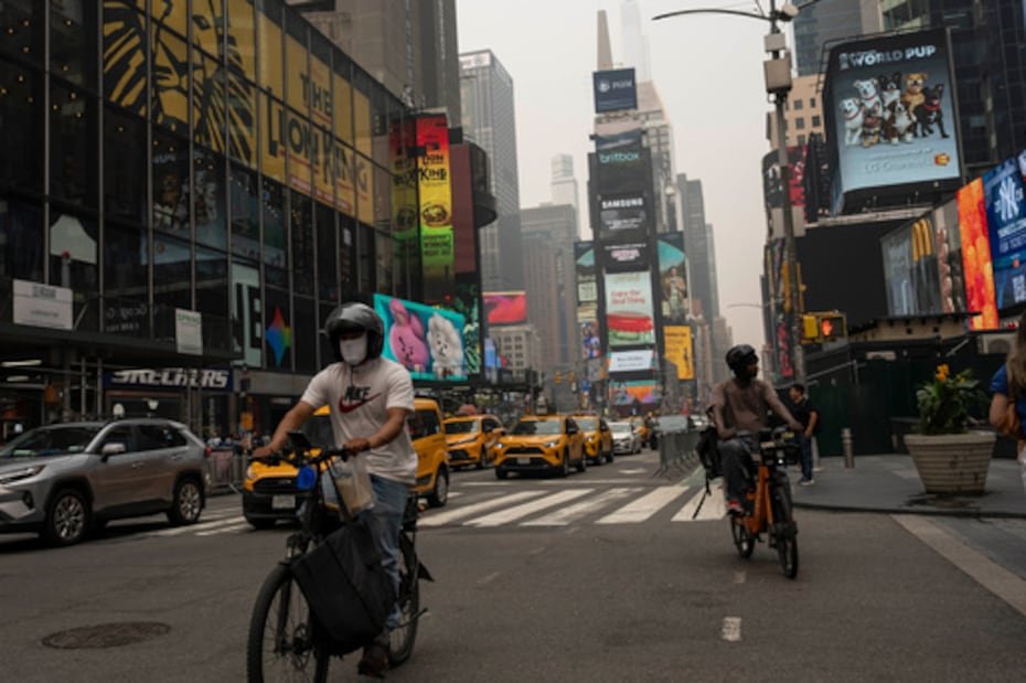 Una persona con mascarilla va en bicicleta por Times Square mientras el humo de los incendios forestales cubre el cielo.
