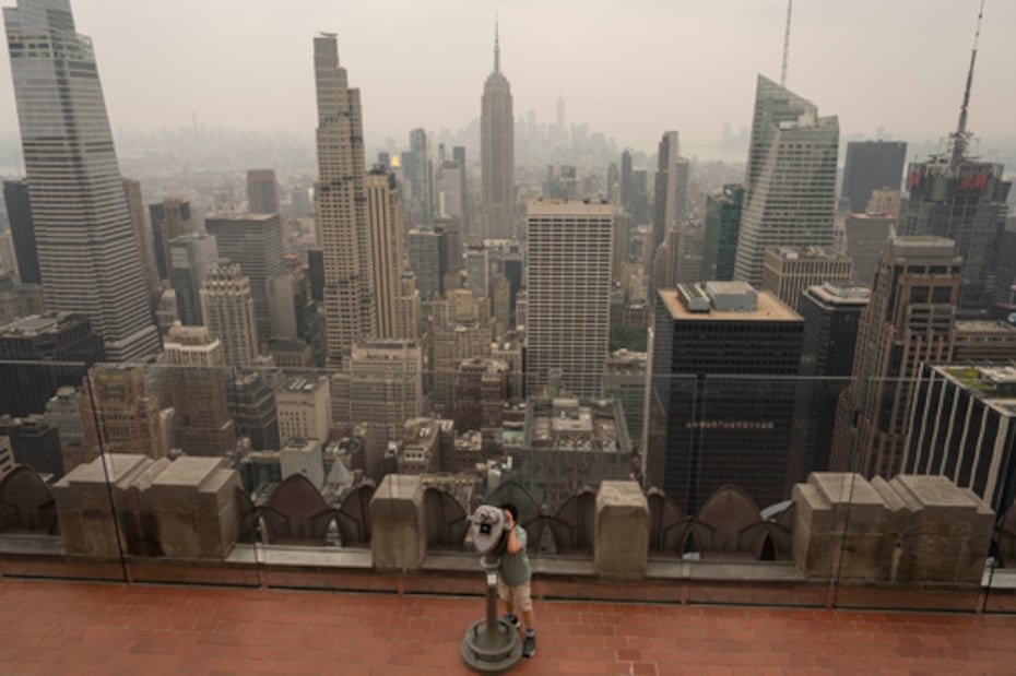 Una persona utiliza unos prismáticos para observar cómo el humo de los incendios forestales cubre el cielo desde el mirador "Top of The Rock" del Rockefeller Center.