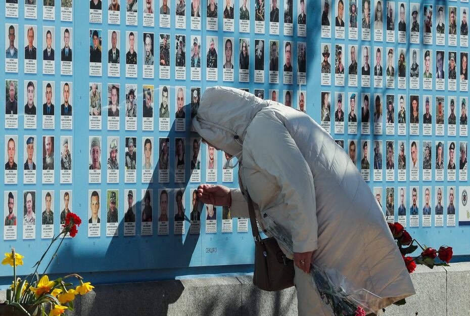 Una mujer toca el retrato de un ser querido mientras familiares, amigos y camaradas observan el Muro de la Memoria que conmemora a los defensores caídos de Ucrania, cerca de la catedral de San Mijaíl en Kiev, Ucrania.